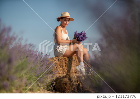 woman sitting in a field of lavender and wearing a straw hat. She is smiling and holding a bouquet of flowers. Scene is peaceful and serene, as the woman is surrounded by the beauty of nature woman sitting in a field of lavender and wearing a straw hat. She is smiling and holding a bouquet of flowers. Scene is peaceful and serene, as the woman is surrounded by the beauty of nature 121172776