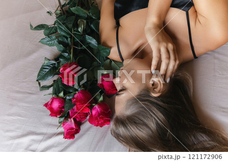 A woman is laying on a bed with a bouquet of red roses next to her. Concept of romance and intimacy, as the woman is surrounded by the flowers and he is in a relaxed and comfortable position. A woman is laying on a bed with a bouquet of red roses next to her. Concept of romance and intimacy, as the woman is surrounded by the flowers and he is in a relaxed and comfortable position. 121172906
