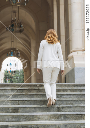 Woman White Suit Stairs - Walking up the stairs of a grand building in a white suit. Woman White Suit Stairs - Walking up the stairs of a grand building in a white suit. 121172926