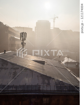 rays of sun lit roofs of urban houses through smog 121174004