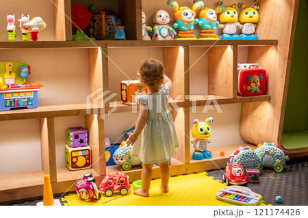 Toddler exploring toy shelves in a colorful playroom. Concept of curiosity and early learning Toddler exploring toy shelves in a colorful playroom. Concept of curiosity and early learning 121174426