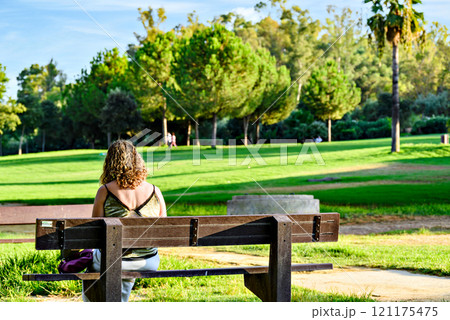 Blonde curly haired woman sitting on a bench in La Retama park in Alcala de Guadaira, Seville, Spain 121175475