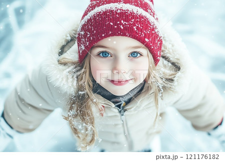 A portrait girl in a white winter jacket and a red hat skates on a winter skating rink 121176182