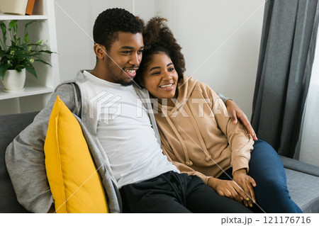 African American couple relaxes on a cozy sofa, sharing a joyful moment while watching a show. Essence of quality time and comfort in a stylish modern living room 121176716