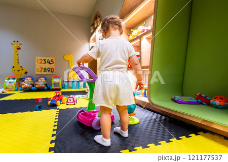 Young child playing on a bright playmat in a toy-filled playroom. Concept of exploration and joyful learning Young child playing on a bright playmat in a toy-filled playroom. Concept of exploration and joyful learning 121177537