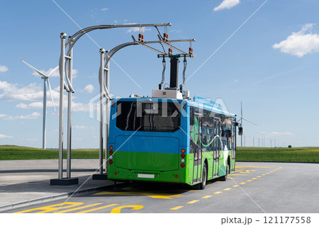 Electric bus at a stop is charged by pantograph. Wind turbines on the horizon 121177558