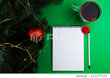 A white banknote and a white pencil with a black lead and a black eraser lie on a green background, next to it is a mug of black tea with a paper red label wishing a Happy New Year, on the left there 121177572