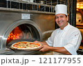 The chef Man smiling at a table with pizza, plant, and cheese in front of him 121177955