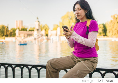 Young peruvian woman using smartphone in madrid's retiro park near the lake 121178301