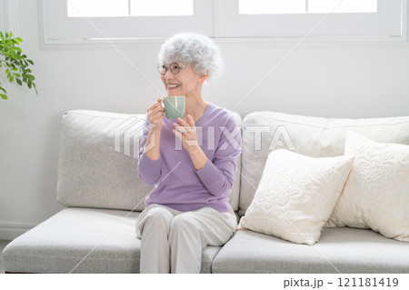 ソファーでコーヒーを飲みながらくつろぐシニア女性 121181419