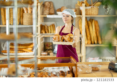 Bakery young woman employee holds basket of ready-made croissant Bakery young woman employee holds basket of ready-made croissant 121181533