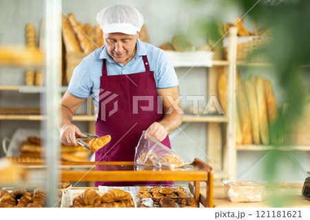 Elderly man seller puts croissants in bag 121181621