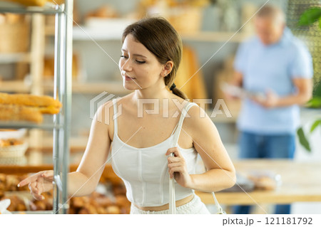 Interested girl looking at baked goods on shelves in display case in bakery store Interested girl looking at baked goods on shelves in display case in bakery store 121181792
