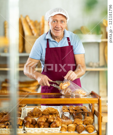 Senior man seller puts croissant in plastic disposable bag for buyer, packs goods. 121181796