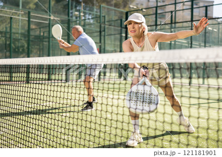 Motivated senior woman playing padel with her teammate in court Motivated senior woman playing padel with her teammate in court 121181901