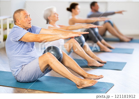 People of different ages doing pilates exercises with fitness ball during group training at fitness studio 121181912