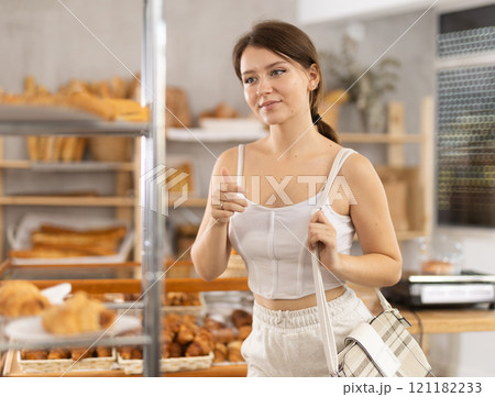 Interested girl looking at baked goods on shelves in display case in bakery store 121182233