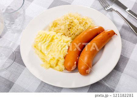 On table there is plate with grilled sausages, sauerkraut and slices of potatoes 121182281