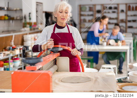 Woman rolling piece of clay on special mechanical machine - craft machine clay press roller 121182284