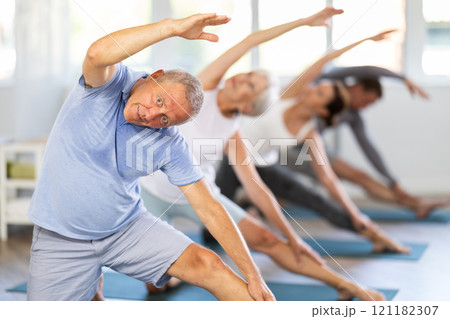 Mature male participant working out practice Parighasana, bolt pose with students group Mature male participant working out practice Parighasana, bolt pose with students group 121182307
