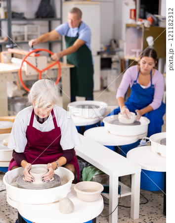 Mature woman learning how to create pottery on potter wheel in workshop 121182312