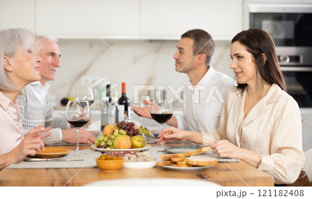 Mature married couple are sitting at table, enjoying food and wine with middle-aged guests. 121182408