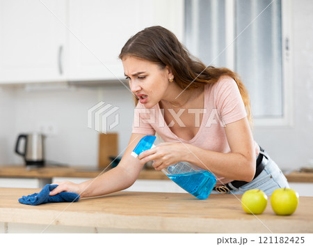 Displeased housewife cleaning dinning table with rag in kitchen Displeased housewife cleaning dinning table with rag in kitchen 121182425