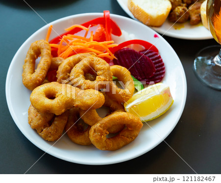 Breaded calamari rings deep fried on white plate with sliced vegetables Breaded calamari rings deep fried on white plate with sliced vegetables 121182467