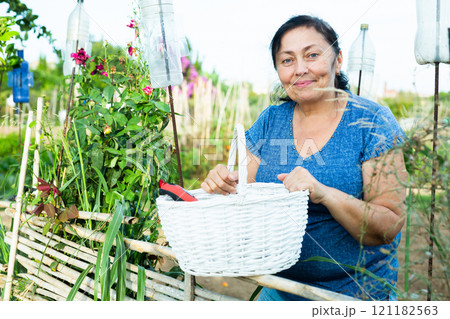 Portrait of an adult woman at wicker fence of her country house on summer day 121182563