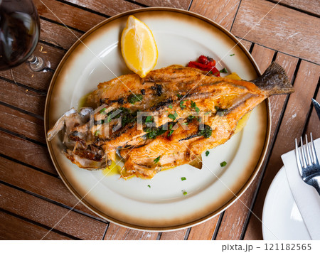 Fried trout carcass, complemented with lemon and edible green 121182565