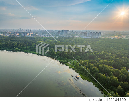 Big lake with green shores in bright sun light and city on horizon, aerial landscape. Recreation concept. Aerial view 121184360