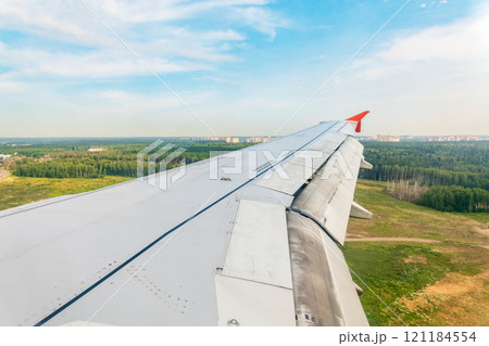 View of airplane wing, blue skies and green land during landing. Airplane window view. View of airplane wing, blue skies and green land during landing. Airplane window view. 121184554
