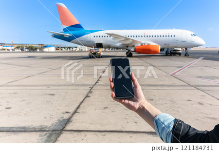 Girl holds a smartphone with a black screen close-up. Phone on the background of the airport with an airplane Girl holds a smartphone with a black screen close-up. Phone on the background of the airport with an airplane 121184731