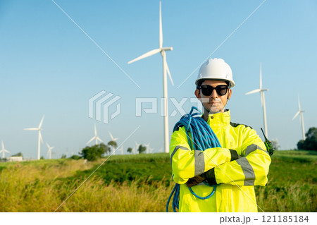 Portrait of wind turbine worker or engineer man stand with arm-crossed and look at camera with row of wind turbine in the background. Portrait of wind turbine worker or engineer man stand with arm-crossed and look at camera with row of wind turbine in the background. 121185184