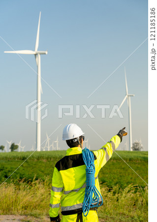 Vertical image of back of wind turbine or windmill engineer worker point to his right side with row of wind turbine in the background. Vertical image of back of wind turbine or windmill engineer worker point to his right side with row of wind turbine in the background. 121185186