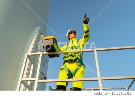 Wind turbine worker or technician man stand on base with toolsbox and point forward to workplace. Wind turbine worker or technician man stand on base with toolsbox and point forward to workplace. 121185192