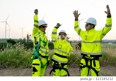 Group of wind turbine workers or technicians raise their hands up together with warm light and row of wind turbine in the background. 121185212