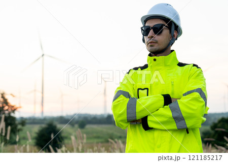 Portrait of wind turbine worker or technician man stand with arm-crossed and look to his right side with row of wind turbine in the background. Portrait of wind turbine worker or technician man stand with arm-crossed and look to his right side with row of wind turbine in the background. 121185217