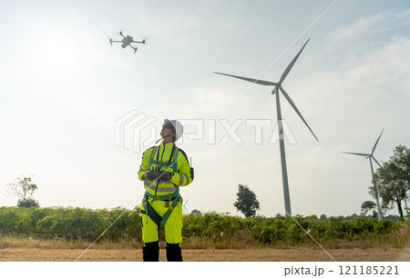Wind turbine or windmill worker man stand and control drone in workplace field with row of wind turbine pole in the background. Wind turbine or windmill worker man stand and control drone in workplace field with row of wind turbine pole in the background. 121185221