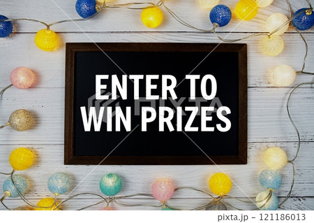 Enter To Win Prizes text written on blackboard with LED cotton balls decoration on wooden background Enter To Win Prizes text written on blackboard with LED cotton balls decoration on wooden background 121186013