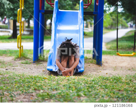 A sad little girl is sitting alone on a playground slide. An unhappy child is playing alone. 121186168