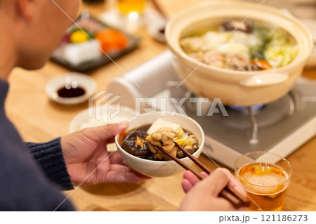 冬の夜のリビングで夕食の鍋料理を楽しむ男性の手元 121186273