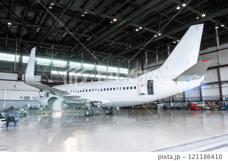 White jet plane in the hangar. Checking mechanical systems for flight operations. Passenger aircraft under maintenance White jet plane in the hangar. Checking mechanical systems for flight operations. Passenger aircraft under maintenance 121186410