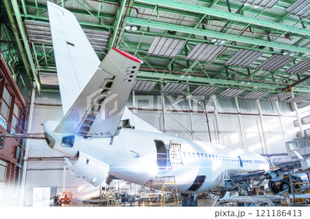 Passenger aircraft under maintenance in the hangar. Checking mechanical systems for flight operations. Close-up view of the tail of the airplane 121186413