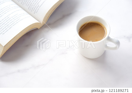 ページを開いた本（洋書）とコーヒーの入ったコーヒーカップで、コーヒーを飲みながら読書を楽しむイメージ 121189271
