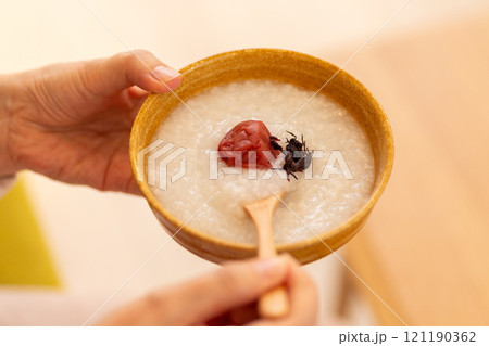 梅干しの乗ったお粥(梅がゆ)を食べる女性の手元 梅干しの乗ったお粥(梅がゆ)を食べる女性の手元 121190362