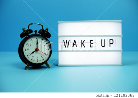 Wake Up letterboard text on LED Lightbox and alarm clock on blue background Wake Up letterboard text on LED Lightbox and alarm clock on blue background 121192365