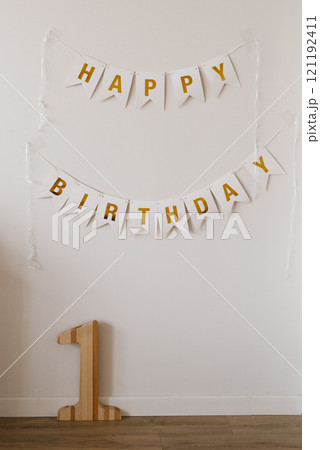 White wall with two banners which says Happy Birthday. Wooden number one on the floor in front of the wall for baby birthday White wall with two banners which says Happy Birthday. Wooden number one on the floor in front of the wall for baby birthday 121192411