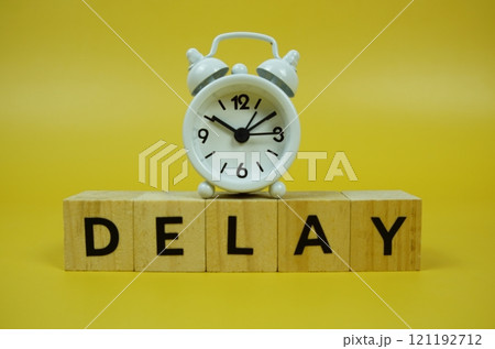 Delay with wooden blocks alphabet letters and alarm clock on yellow background Delay with wooden blocks alphabet letters and alarm clock on yellow background 121192712