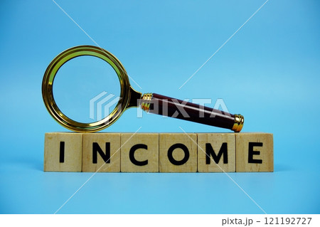 Income with wooden blocks alphabet letters and Magnifying glass on blue background 121192727